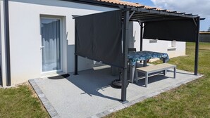 Un espacio al aire libre cubierto con una mesa, bancos, una puerta y un edificio con tejado de tejas.