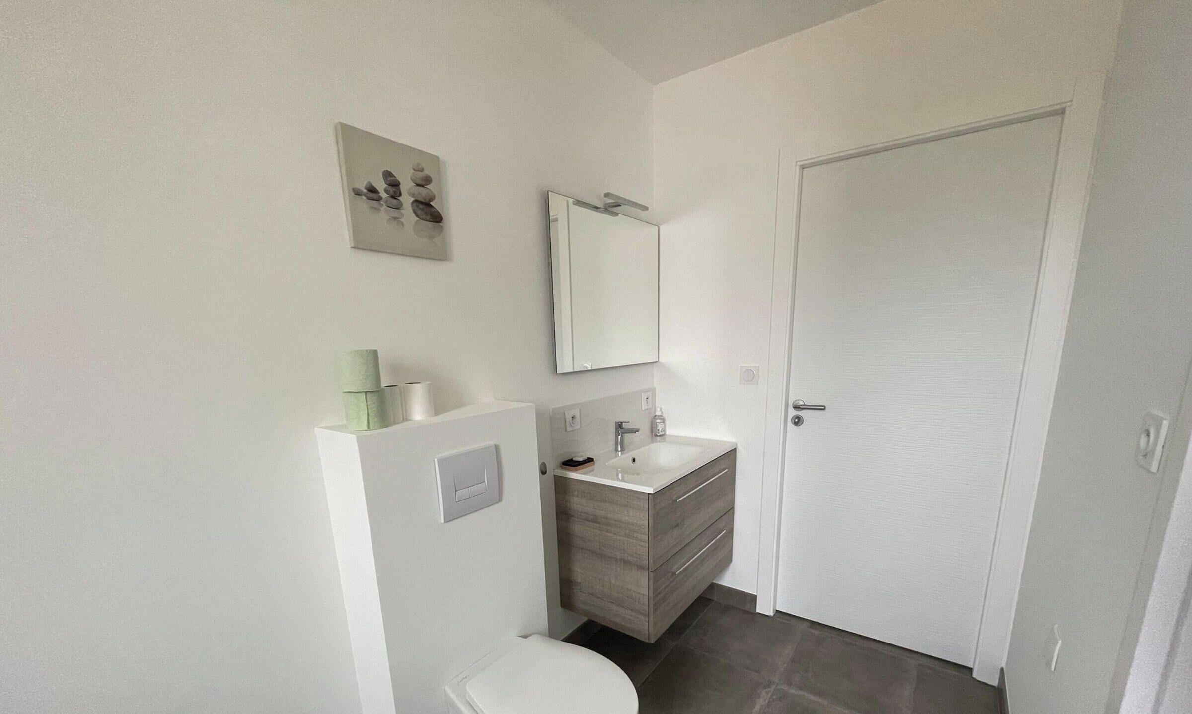A bathroom with a toilet, sink, mirror, and a door.