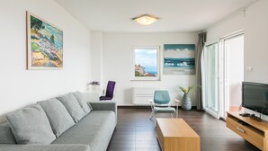 A modern living room with a grey sofa, a wooden coffee table, a TV, and a painting of a landscape.