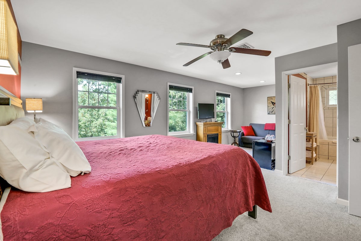 A bedroom with a large bed, a ceiling fan, and multiple windows.