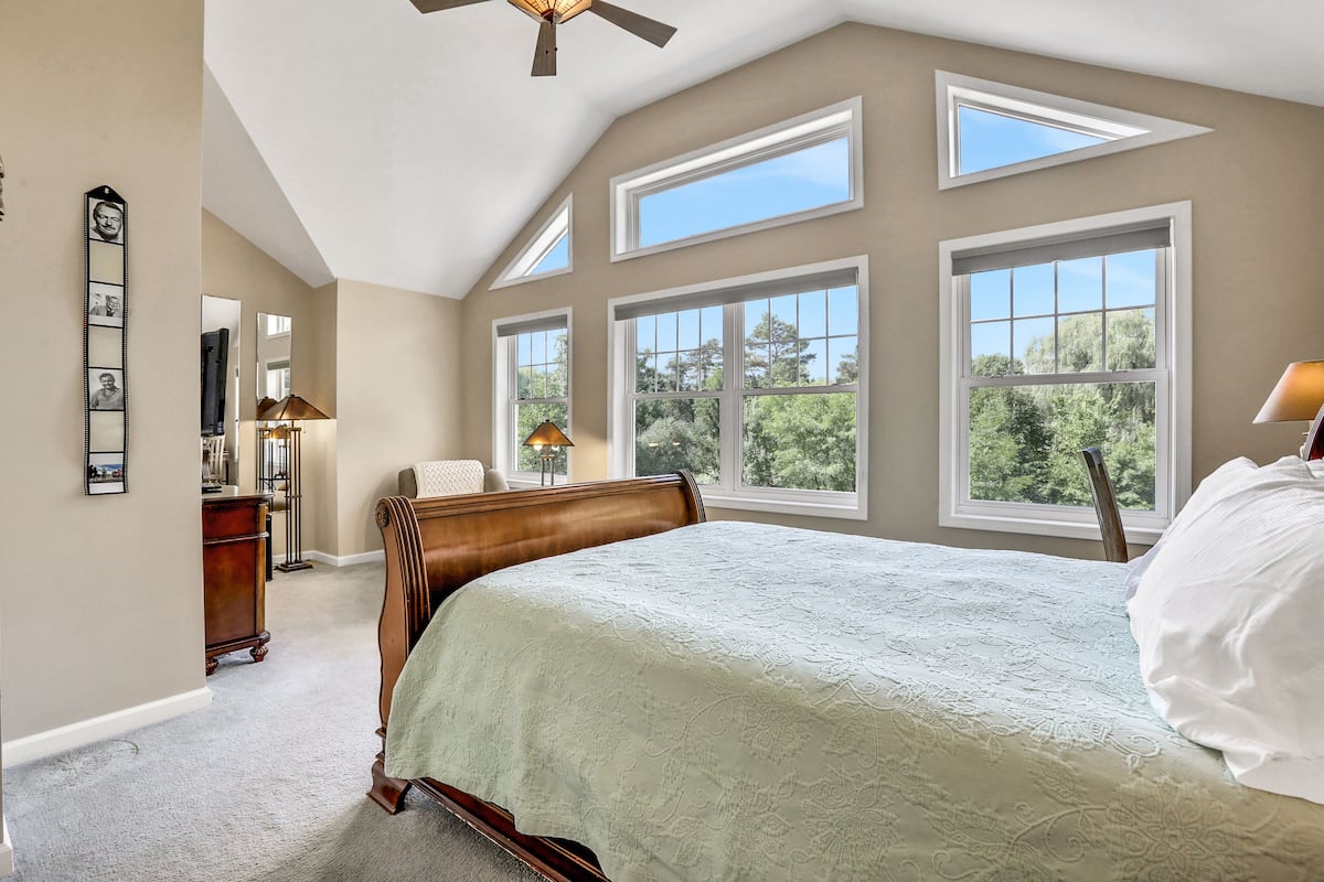 A bedroom with a large bed, multiple windows, a ceiling fan, and a dresser.