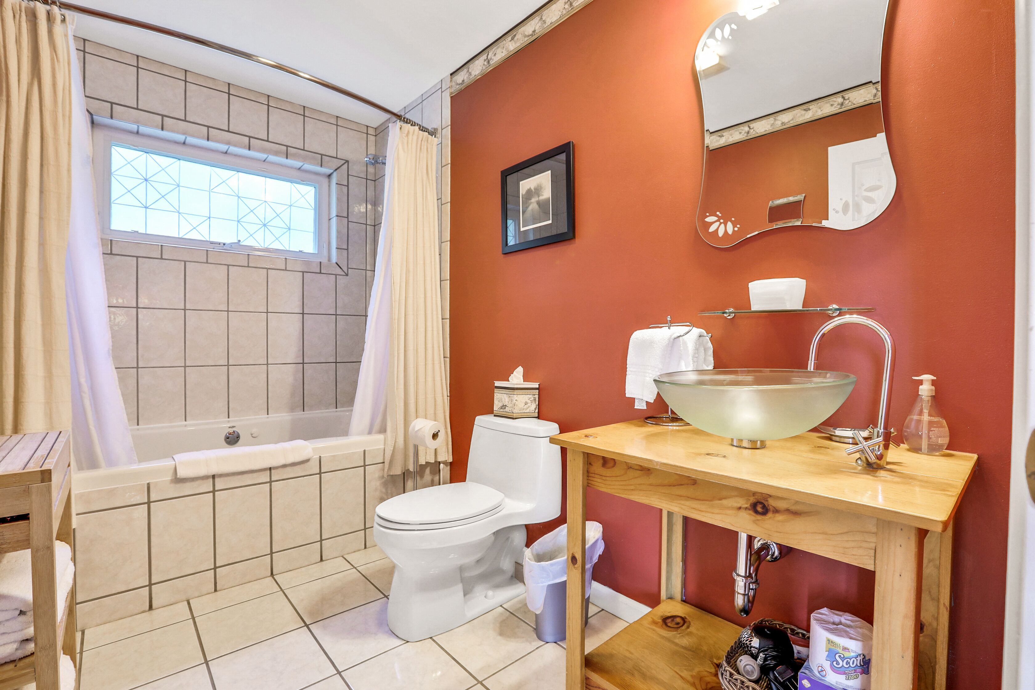 Un bagno con vasca, WC, lavandino e una finestra con tenda.