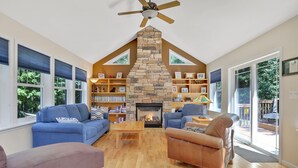 A living room with a stone fireplace, blue sofas, a wooden coffee table, and a ceiling fan. - Moondance Ridge Bed & Breakfast (New Paltz)