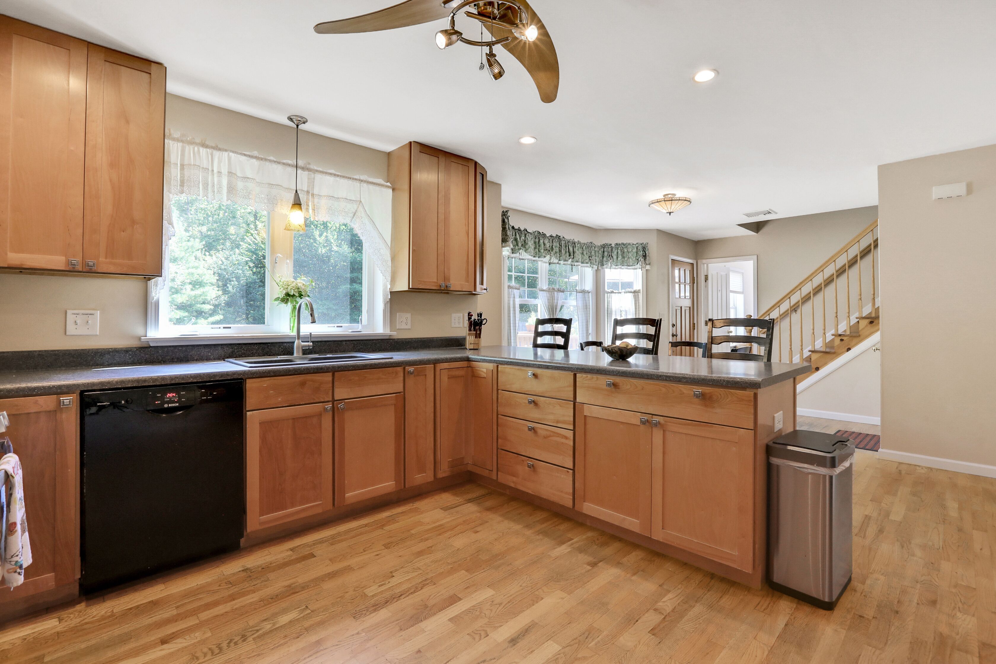 A kitchen with wooden cabinets, a dishwasher, a sink, and a trash can.