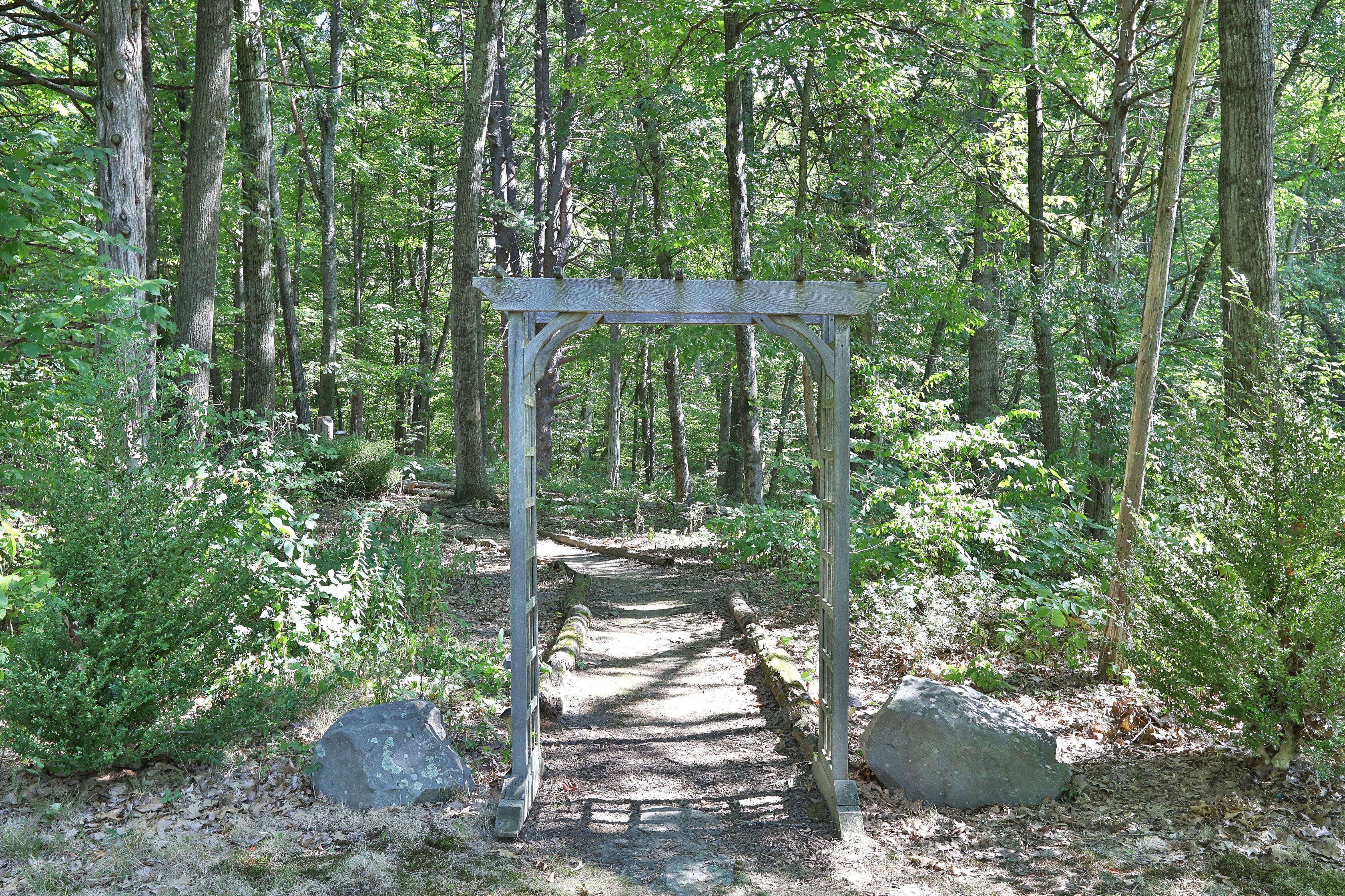 Ein hölzerner Kletterbogen mit einem Steinweg, der durch einen Wald führt.