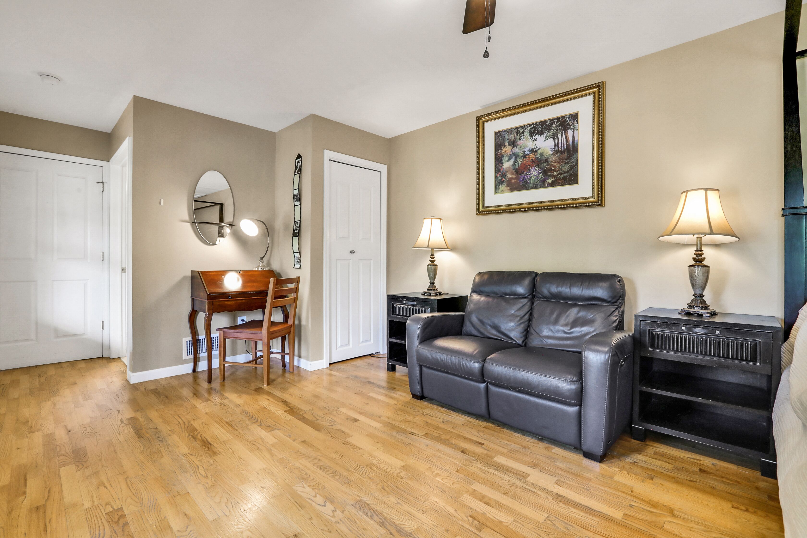 A living room with hardwood flooring, a leather sofa, a wooden chair, a dining table, and two lamps.