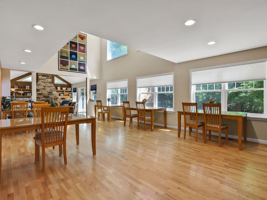 A spacious dining area with wooden tables and chairs, a stone fireplace, and large windows offering views of greenery.
