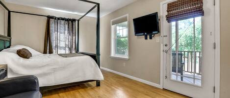 A bedroom with a four-poster bed, a ceiling fan, a television mounted on the wall, and a sliding glass door leading to an outdoor area.