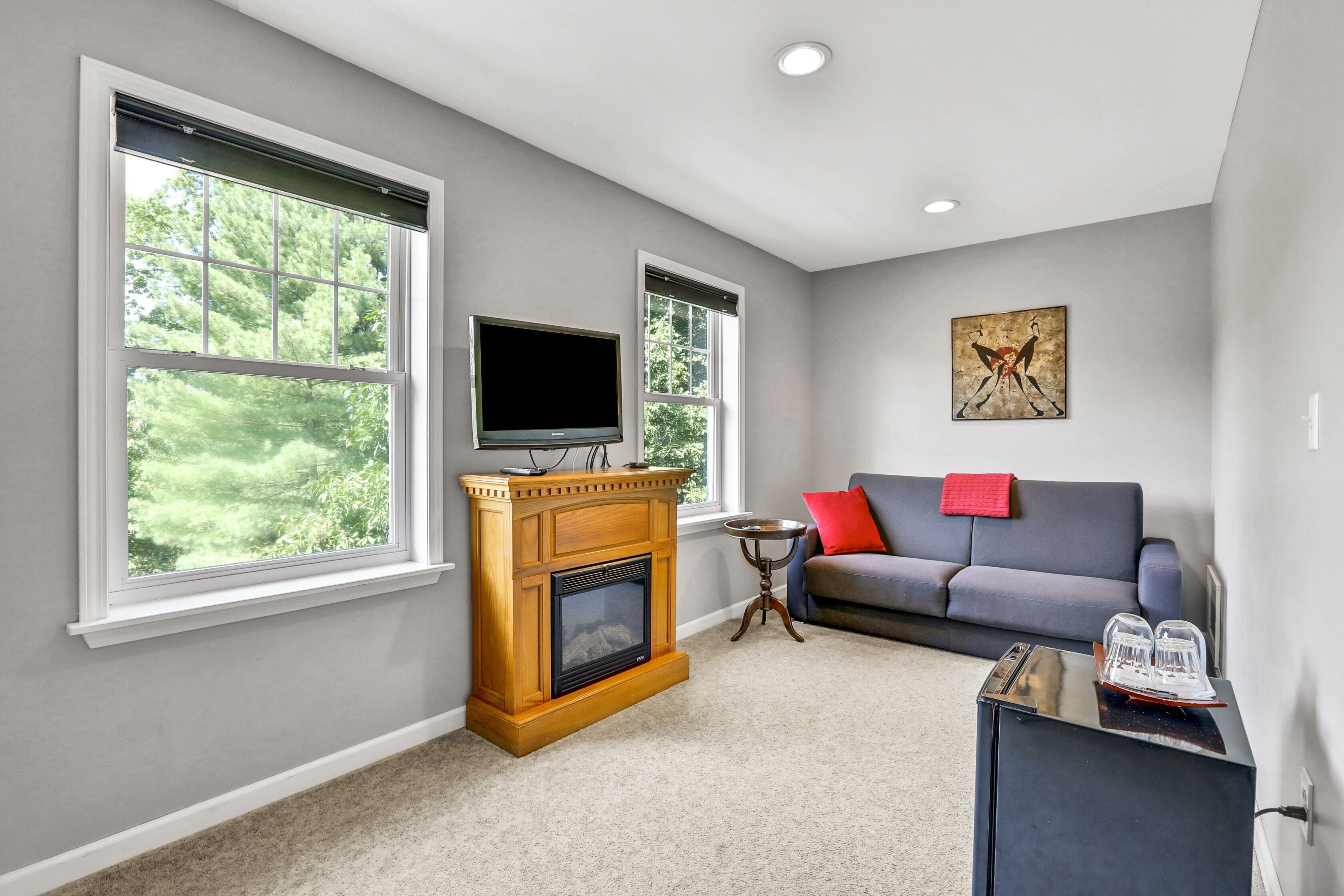 A living room with a fireplace, a television, a couch, and large windows.