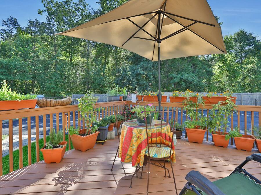 A wooden deck with a table and chairs under a large umbrella, surrounded by potted plants.