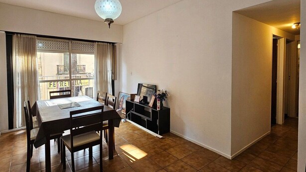 A spacious living area with a dining table, chairs, a TV stand, and a large window with curtains. - Exquisito 3 ambientes Congreso (Buenos Aires)