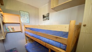 Ein Etagenbett mit blauer Matratze, ein kleiner Holzschemel, ein Bücherregal und ein Wandposter.