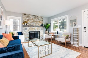 A modern living room with a fireplace, a blue sofa, a glass coffee table, and a white armchair. - Backyard Vibes-Walk to ND-Dogs Welcome-BBall Hoop-Fire Pit-Sleeps 12-2024 Reno (South Bend)