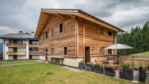 Een houten chalet met schuin dak, een balkon en een terras met buitenmeubilair.