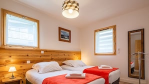Een hotelkamer met twee bedden, houten hoofdborden, een klein nachtkastje met een lamp, een spiegel en een schilderij aan de muur.