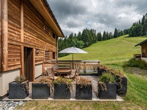 Een houten chalet met een terras, inclusief een tafel en stoelen, omgeven door plantenbakken met beplanting.