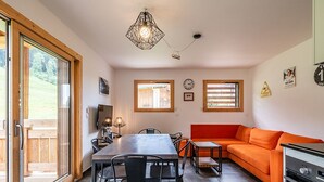 Een moderne keuken met een ingebouwde oven, een eethoek met tafel en stoelen, en een fel oranje bank.