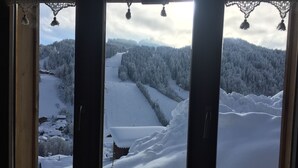 Une fenêtre donnant sur un paysage enneigé, avec une forêt et une colline recouverte de neige.