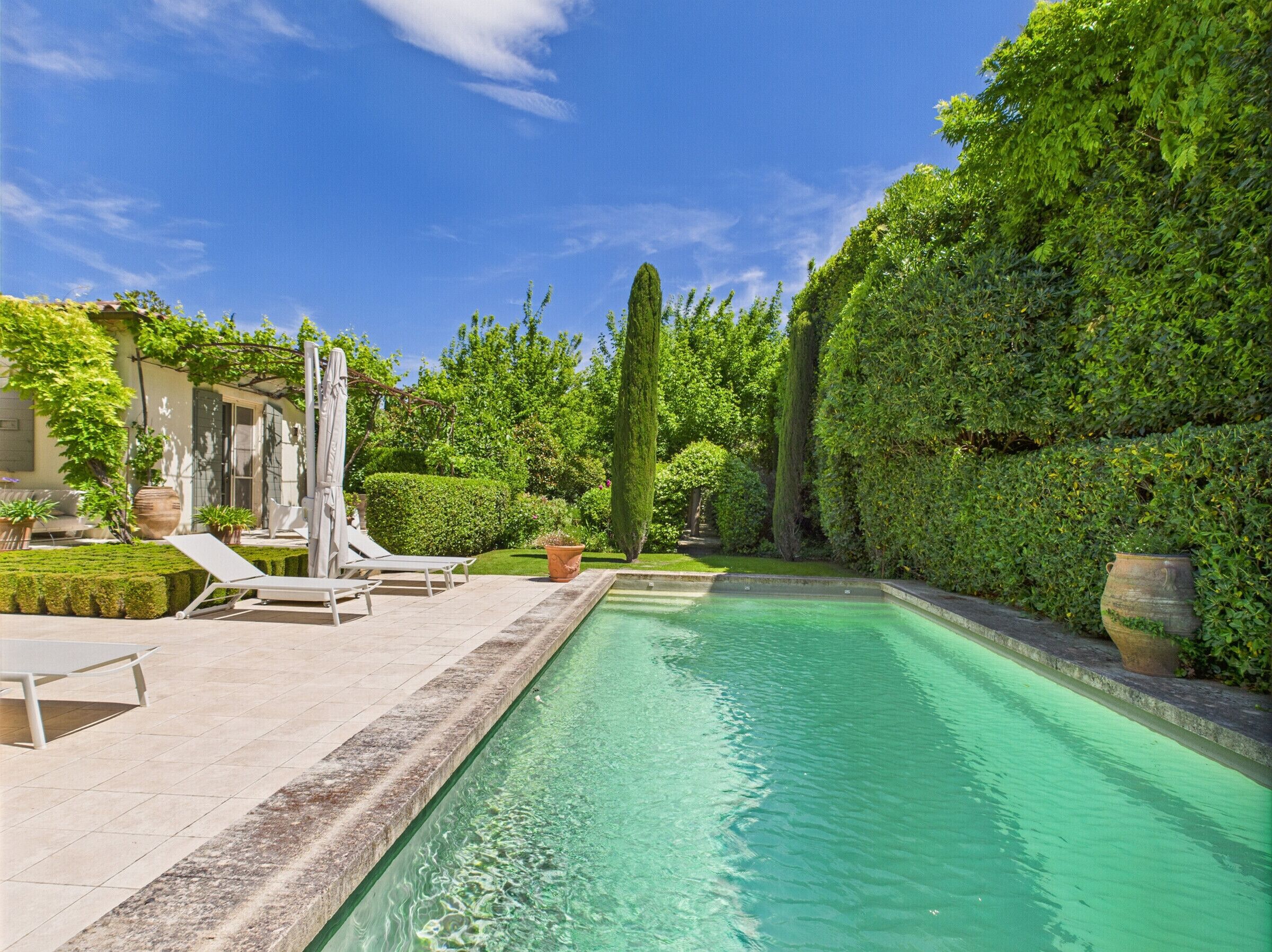 Une piscine rectangulaire à l’eau claire, entourée d’une terrasse dallée agrémentée de chaises longues et de plantes en pot.