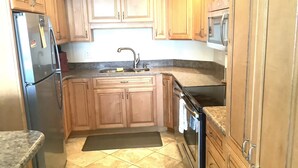 A compact kitchen with wooden cabinets, a stainless steel refrigerator, a microwave, and a sink. - Oceanfront Beautiful Views 2 Bd and 2 Baths Family-Friendly Lovely Furnishings (Myrtle Beach)