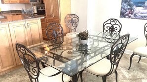 A dining area with a glass-top table surrounded by four chairs with black metal frames and white cushions. There is a potted plant on the table. - Oceanfront Beautiful Views 2 Bd and 2 Baths Family-Friendly Lovely Furnishings (Myrtle Beach)