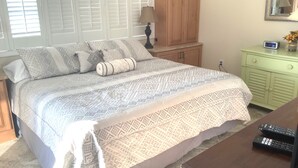 A neatly made bed with patterned bedding, a bedside table with a lamp, a small cabinet, and a clock on the wall. - Oceanfront Beautiful Views 2 Bd and 2 Baths Family-Friendly Lovely Furnishings (Myrtle Beach)