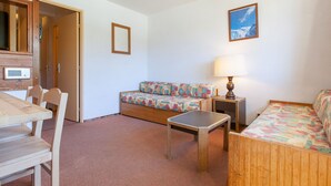 A room with a wooden dining table, two wooden chairs, a sofa, a small wooden table, a lamp, and a picture on the wall.