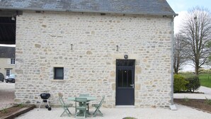 Un edificio de piedra con una puerta, un ventanal pequeño y una mesa con sillas en frente.