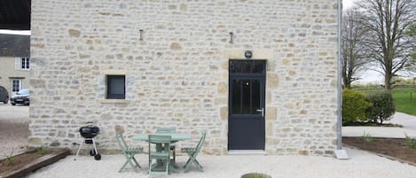 A stone building with a door, a small window, and a table with chairs in front.
