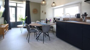 Una cocina moderna con una isla central, zona de comedor con sillas, lámparas colgantes y un amplio ventanal.