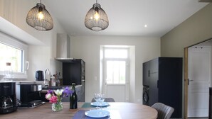 Una cocina moderna con una isla central, dos lámparas colgantes y un comedor con sillas y una mesa para dos.