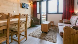 Une pièce chaleureuse avec des murs en bois, un téléviseur fixé au mur, un canapé, un fauteuil, une petite table et une fenêtre avec des rideaux.