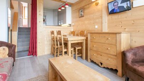 Un intérieur en bois comprenant une table à manger, des chaises, un canapé, un téléviseur et un escalier menant à une autre pièce.