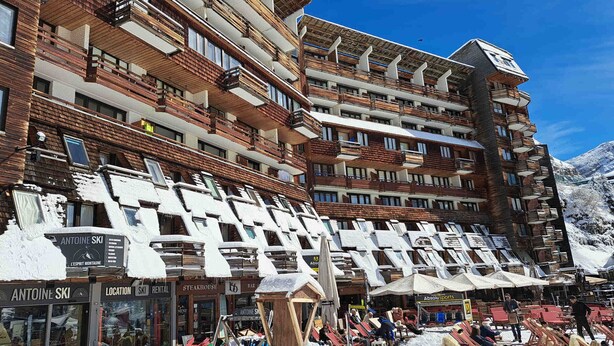 Un hôtel à plusieurs étages, doté de balcons et d’un espace de location de matériel de ski situé à l’avant.