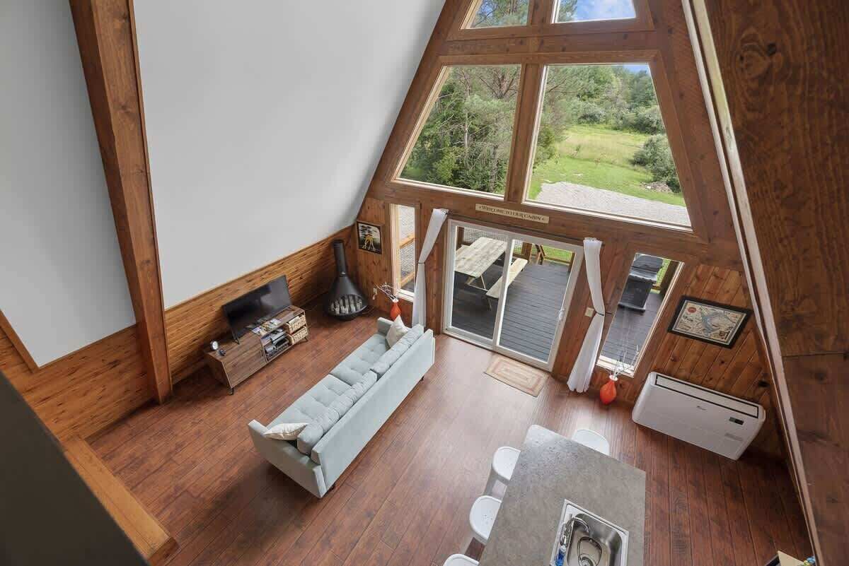 A loft-style room with a large window, wooden beams, a sofa, a dining table, and a fireplace.