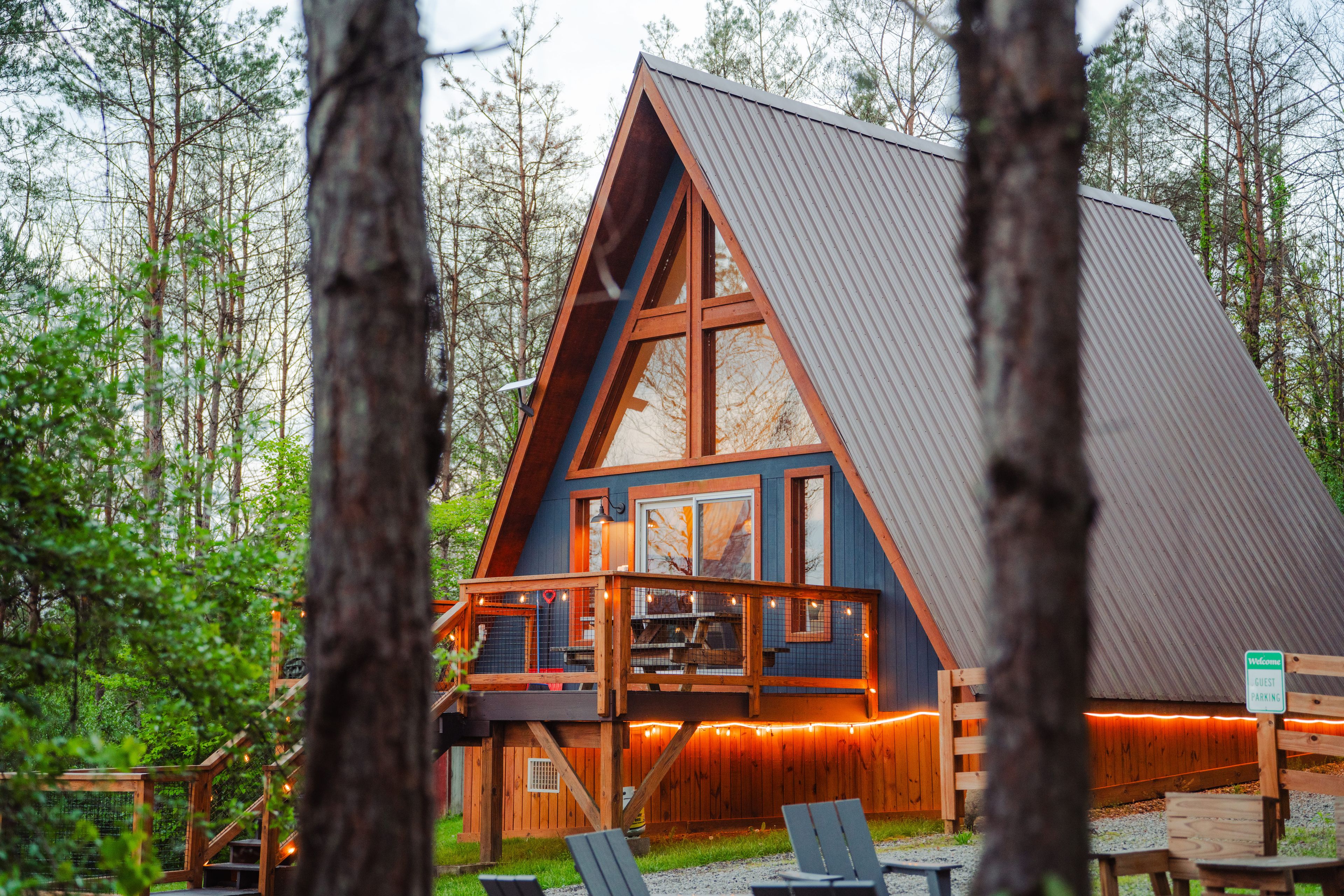 Une cabane avec un toit en pente, une terrasse en bois et un panneau indiquant les places de stationnement réservées aux invités.