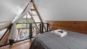 Una camera da letto con soffitto a falde, una testiera in legno, un letto con copripiumino grigio e una finestra vista su un patio.