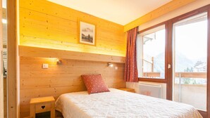 A wooden-paneled bedroom with a bed, a nightstand, and a window with a view of mountains.