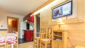 A cozy wooden interior with a dining area, a kitchen, and a television mounted on the wall.