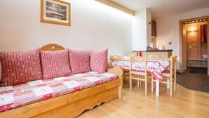 A cozy room with a wooden sofa, a dining table with chairs, and a kitchen area.