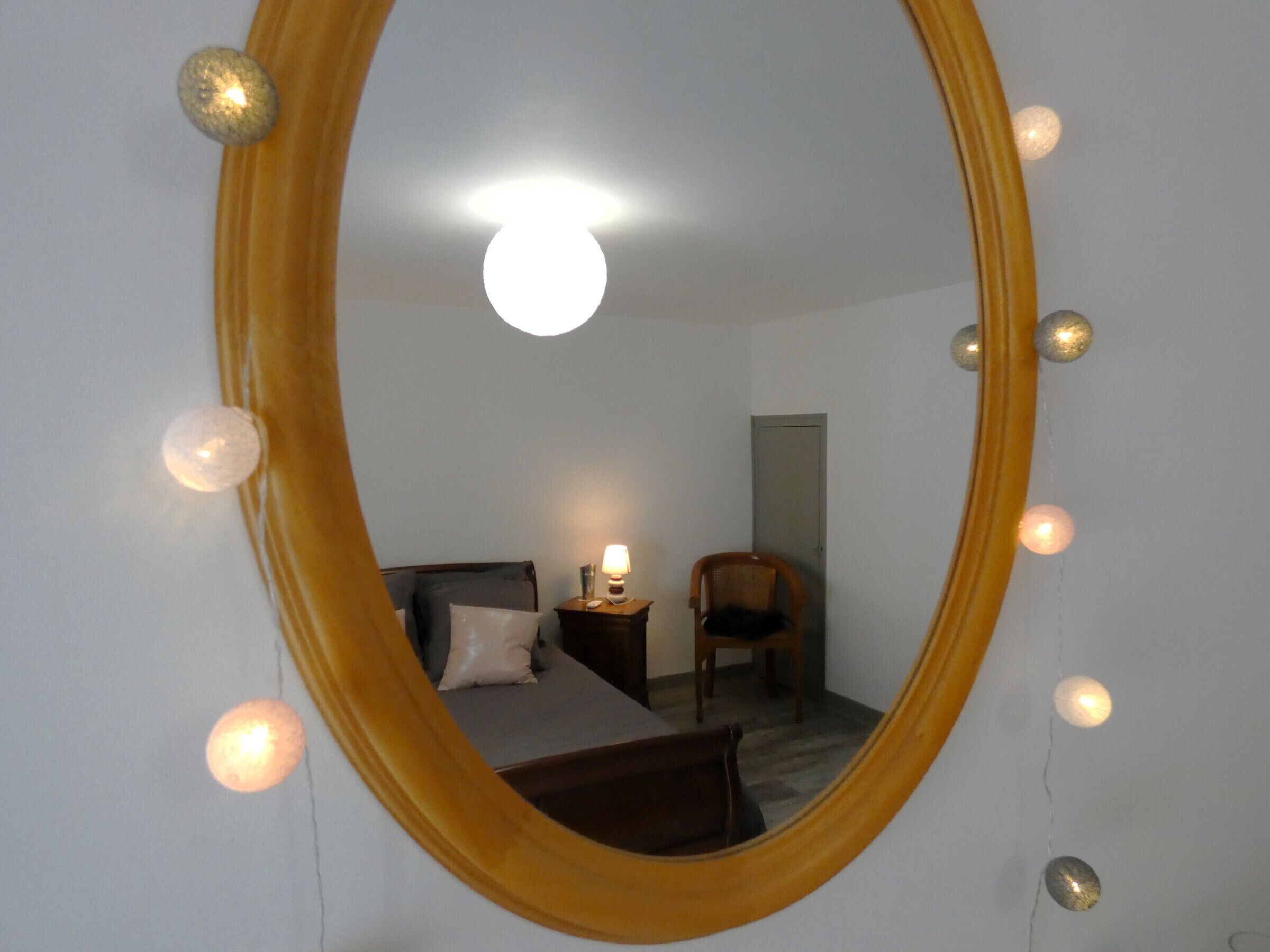 Une chambre avec un grand miroir ovale, un lit avec des oreillers, une table de chevet avec une lampe et une chaise.