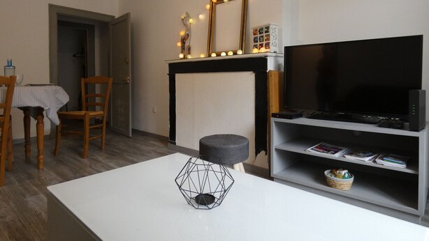 Una sala de estar con televisor, chimenea con luces, mesa de comedor con sillas y una mesa de centro con un objeto geométrico.