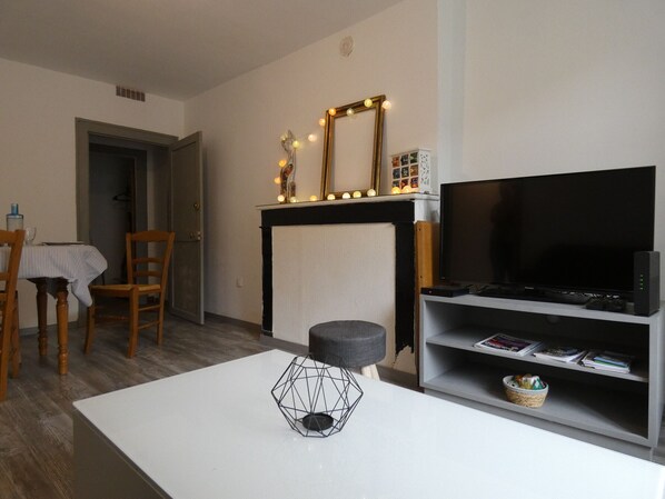 Ein Wohnzimmer mit Fernseher, Kamin mit Beleuchtung, Esstisch mit Stühlen und Couchtisch mit einem geometrischen Objekt.
