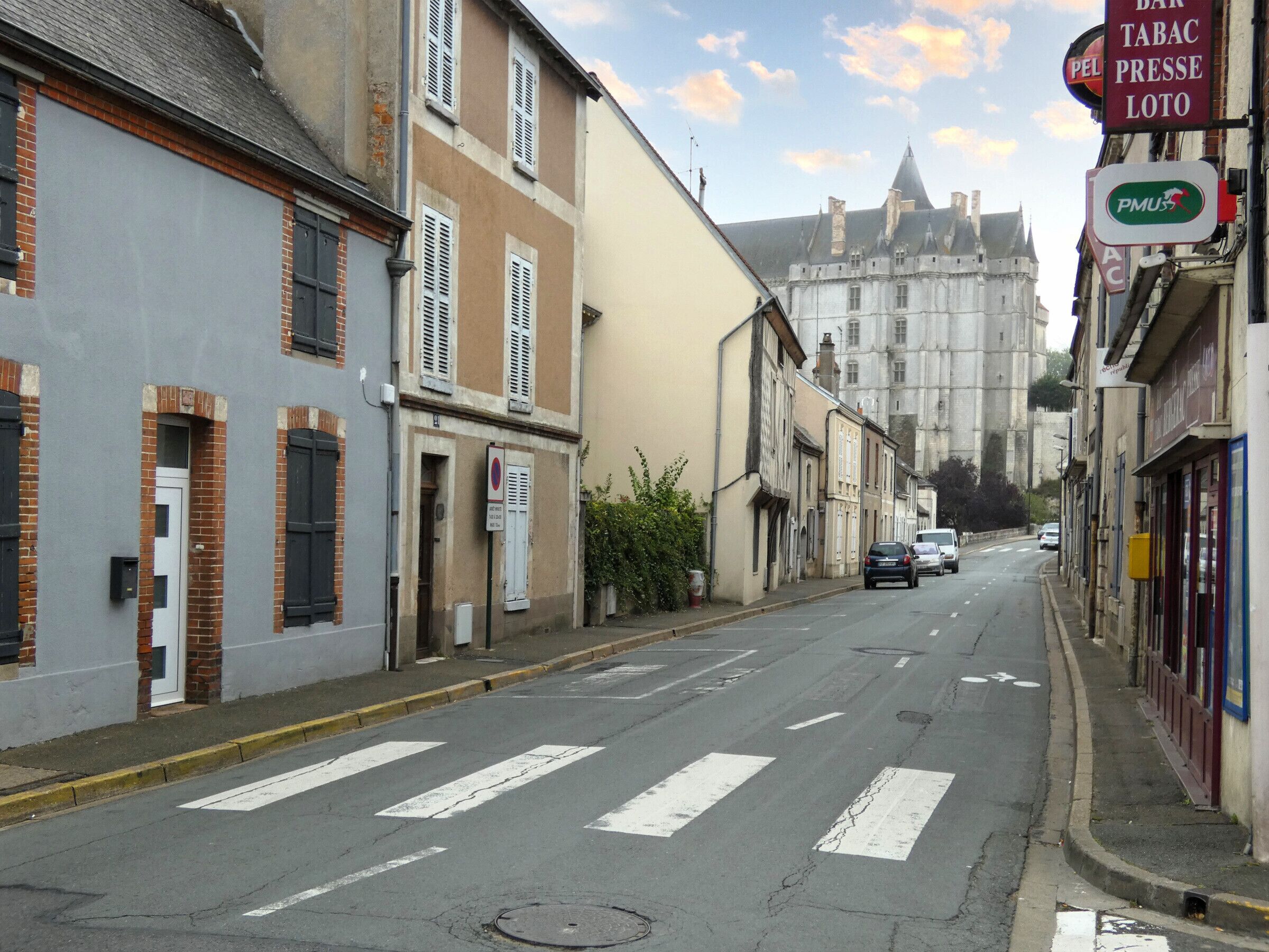 Una strada fiancheggiata da edifici, un segnale di divieto di sosta e un castello in lontananza.