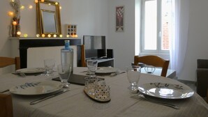 Un comedor con una mesa dispuesta para cuatro, televisión, chimenea y una ventana con cortinas.