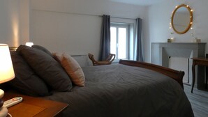 Una habitación de hotel con cama, una silla, una mesa con lámpara, un espejo y chimenea.