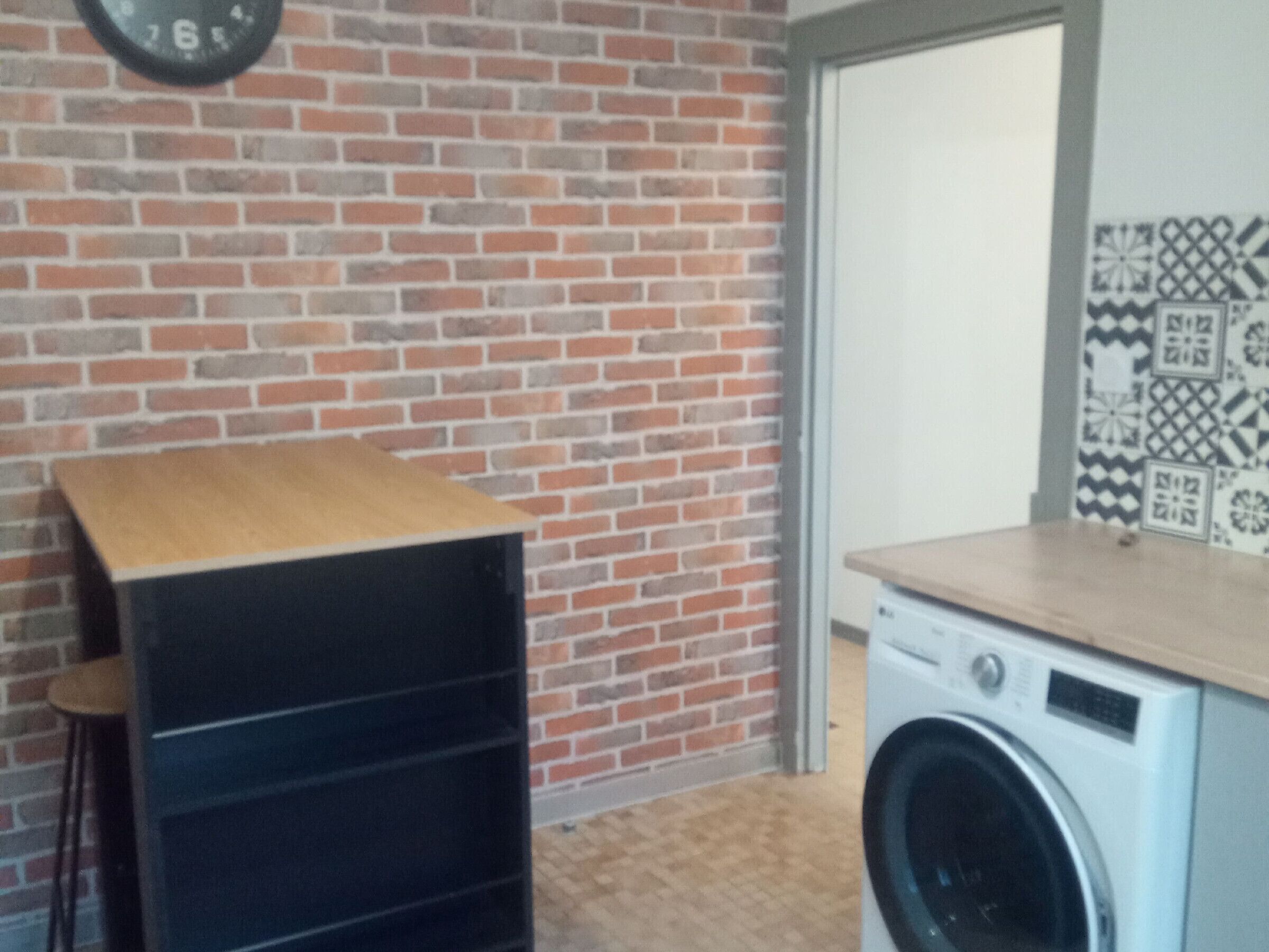 Una habitación con pared de ladrillo, lavadora y estante de madera.
