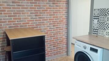 Una habitación con pared de ladrillo, lavadora y estante de madera.