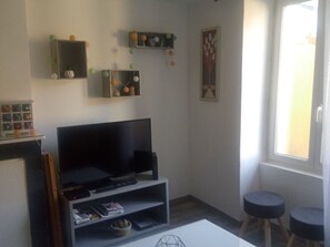 A living room with a flat-screen TV, shelves with decorative items, a coffee table, and a window with a view.