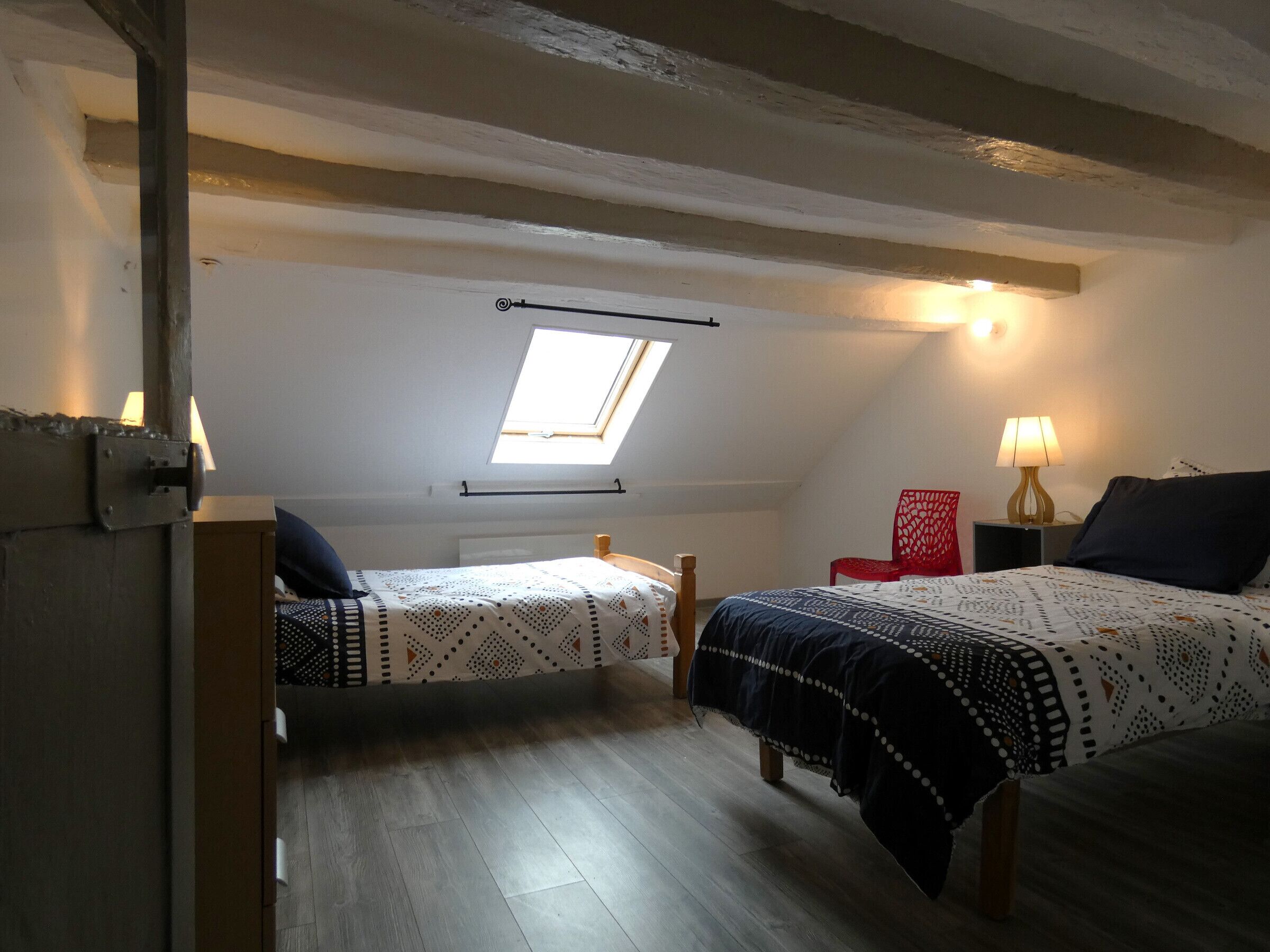 Ein kleines, gemütliches Schlafzimmer im Dachgeschoss mit zwei Betten, einem Dachfenster und einem roten Sessel.